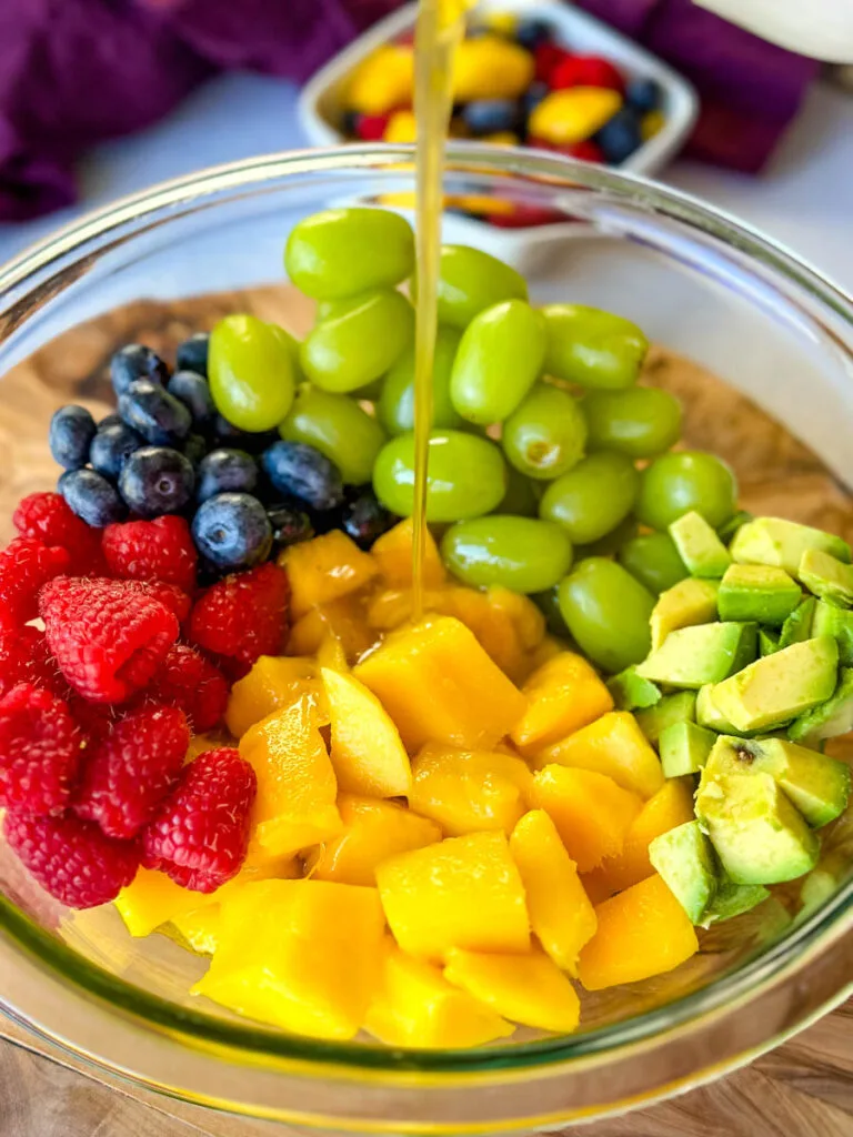 raspberries, blueberries, grapes, and avocado in a glass bowl drizzled with honey lime dressing