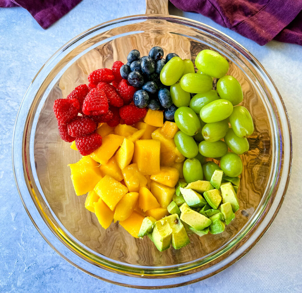 raspberries, blueberries, grapes, and avocado in a glass bowl