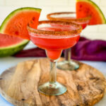 watermelon margaritas on the rocks in a glass with Tajin lined rim and fresh watermelon