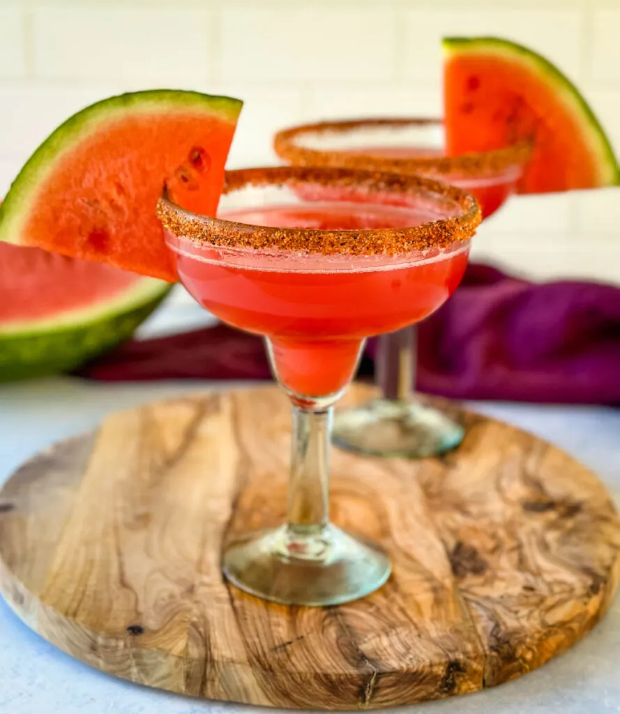 watermelon margaritas on the rocks in a glass with Tajin lined rim and fresh watermelon