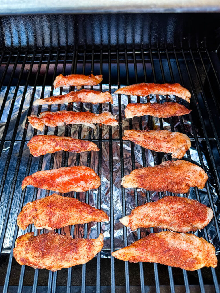 raw seasoned chicken tenders on a Traeger smoker grill
