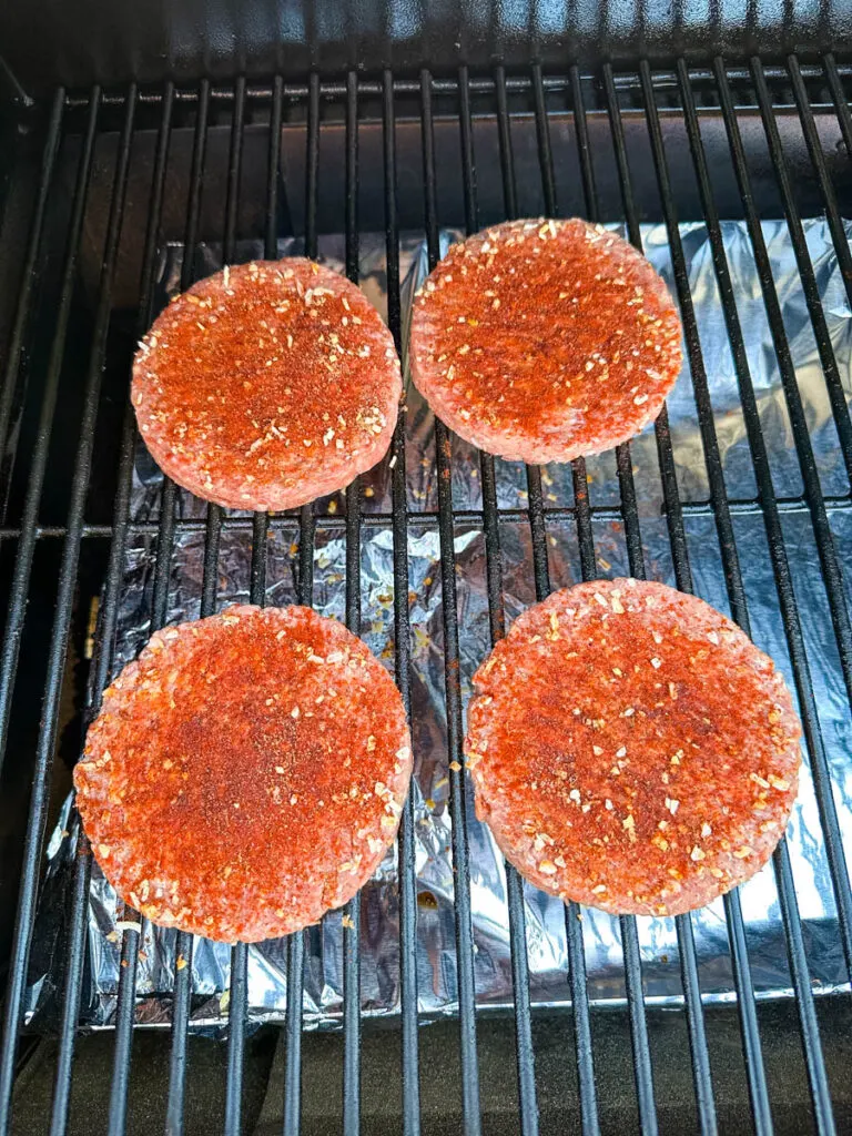raw, seasoned burgers on a Traeger smoker grill