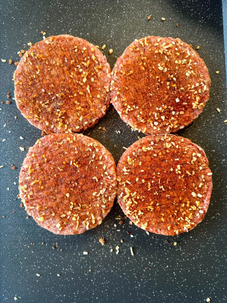 raw seasoned burgers on a flat surface