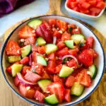 watermelon salad with feta, basil, cucumbers, avocado, strawberries, onion, and balsamic lime dressing in a white bowl