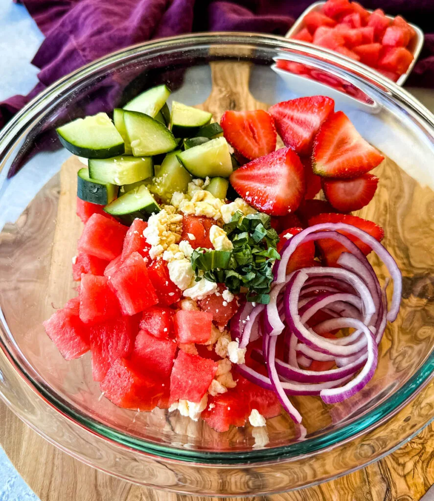 watermelon salad with feta, cucumbers, avocado, basil, strawberries, onion, and balsamic lime dressing in a glass bowl
