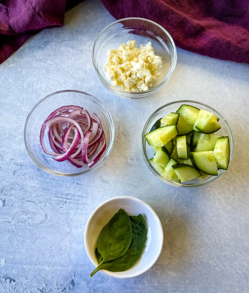 red onions, feta, cucumbers, and fresh basil in separate glass bowls