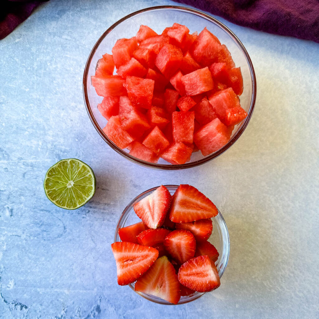 diced watermelon, sliced strawberries, and a lime in separate glass bowls