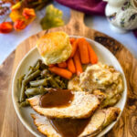 sliced bone in turkey breast on a plate with gravy, mashed potatoes, green beans, carrots, and biscuits