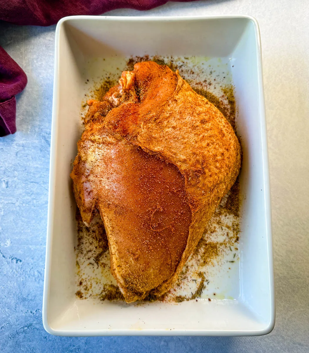 raw seasoned bone in turkey breast in a white 9x13 baking dish