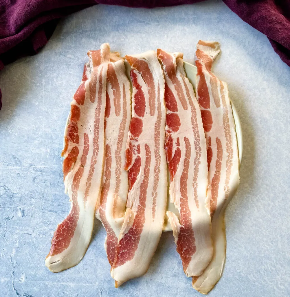 5 slices of uncooked bacon on a plate