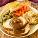 boneless turkey breast slices on a plate with mashed potatoes, gravy, green beans, carrots, and a biscuit