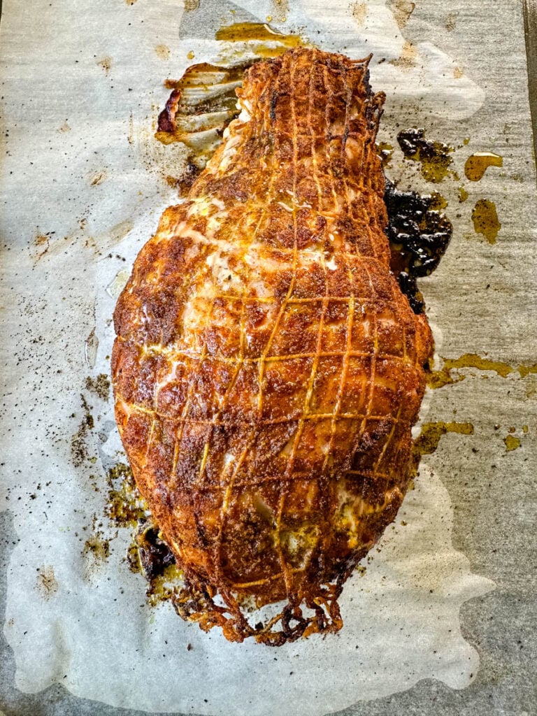 baked roasted boneless turkey breast wrapped in a net on a parchment paper lined sheet pan