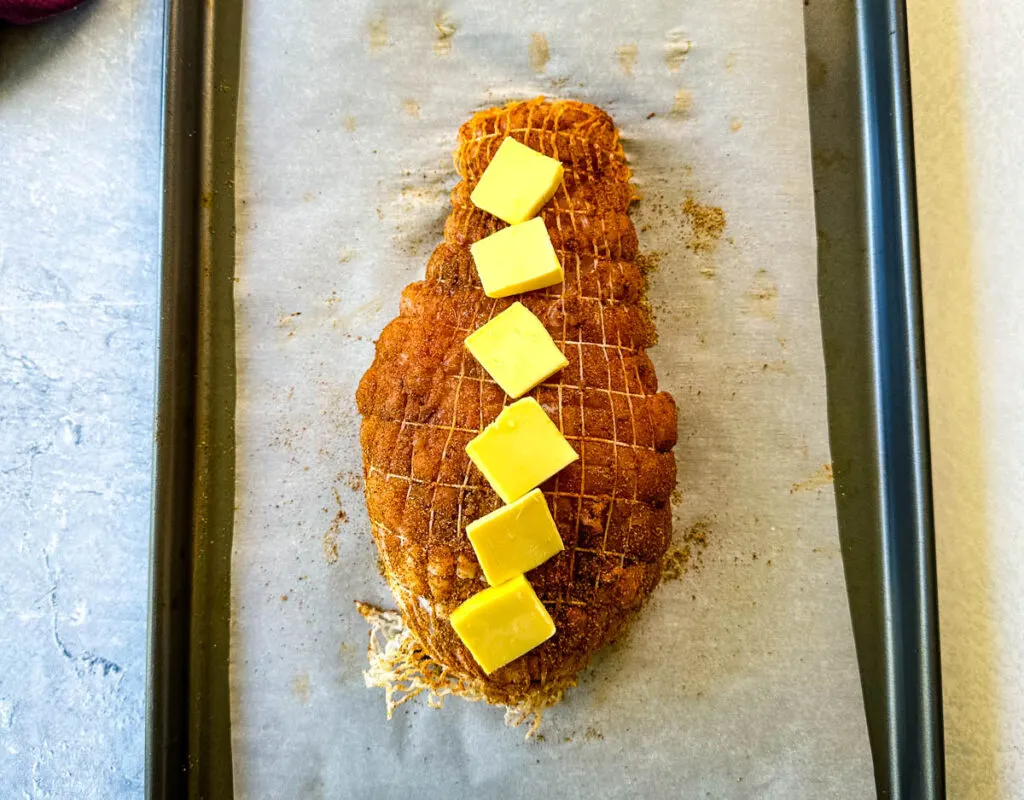 raw, seasoned boneless turkey breast topped with butter wrapped in a net on a parchment paper lined sheet pan