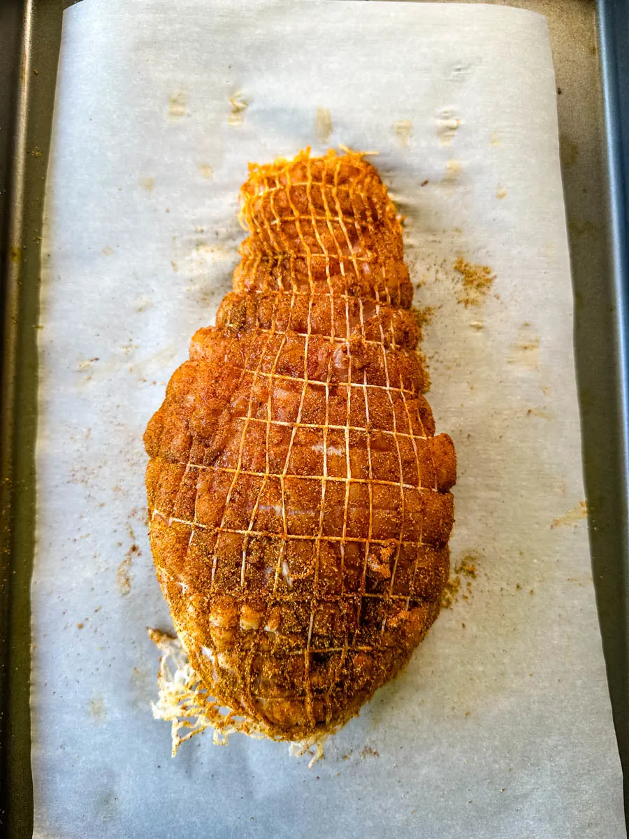 raw, seasoned boneless turkey breast wrapped in a net on a parchment paper lined sheet pan