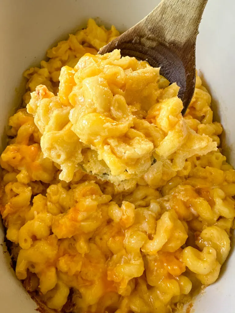 cheddar cheese mac and cheese in a Crockpot slow cooker with a wooden spoon