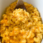cheddar cheese mac and cheese in a Crockpot slow cooker with a wooden spoon