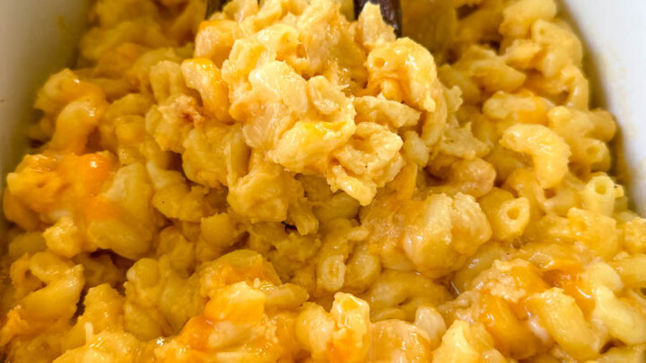 cheddar cheese mac and cheese in a Crockpot slow cooker with a wooden spoon