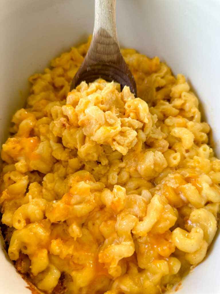 cheddar cheese mac and cheese in a Crockpot slow cooker with a wooden spoon