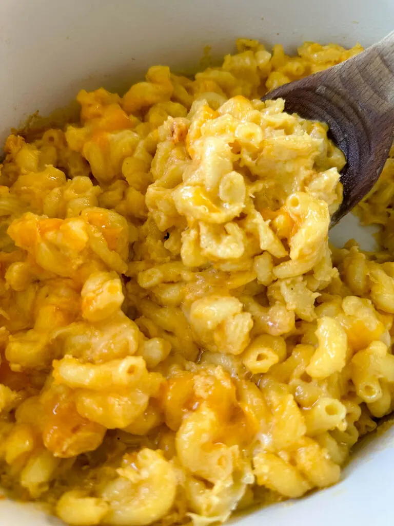 cheddar cheese mac and cheese in a Crockpot slow cooker with a wooden spoon