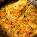 a spoonful of cheesy au gratin potatoes with bacon in a cast iron skillet