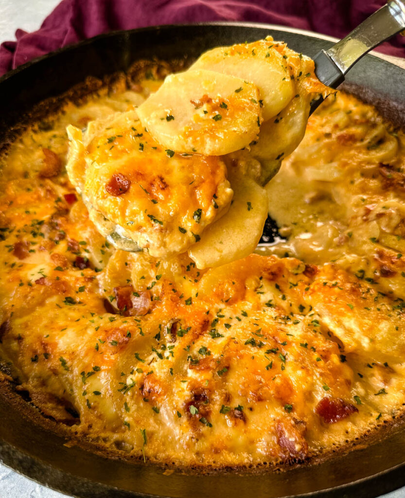 a spoonful of cheesy au gratin potatoes with bacon in a cast iron skillet