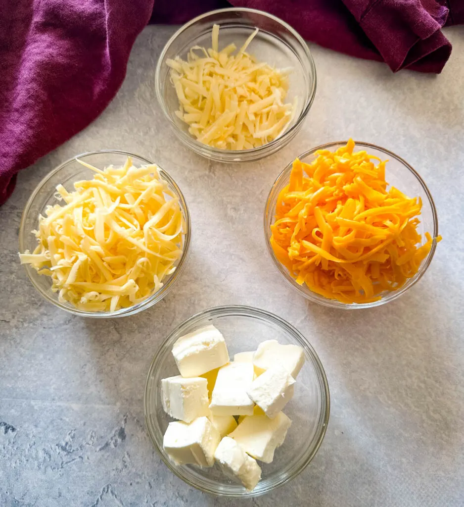 shredded cheddar, Gruyere, Parmesan, and cream cheese in separate glass bowls