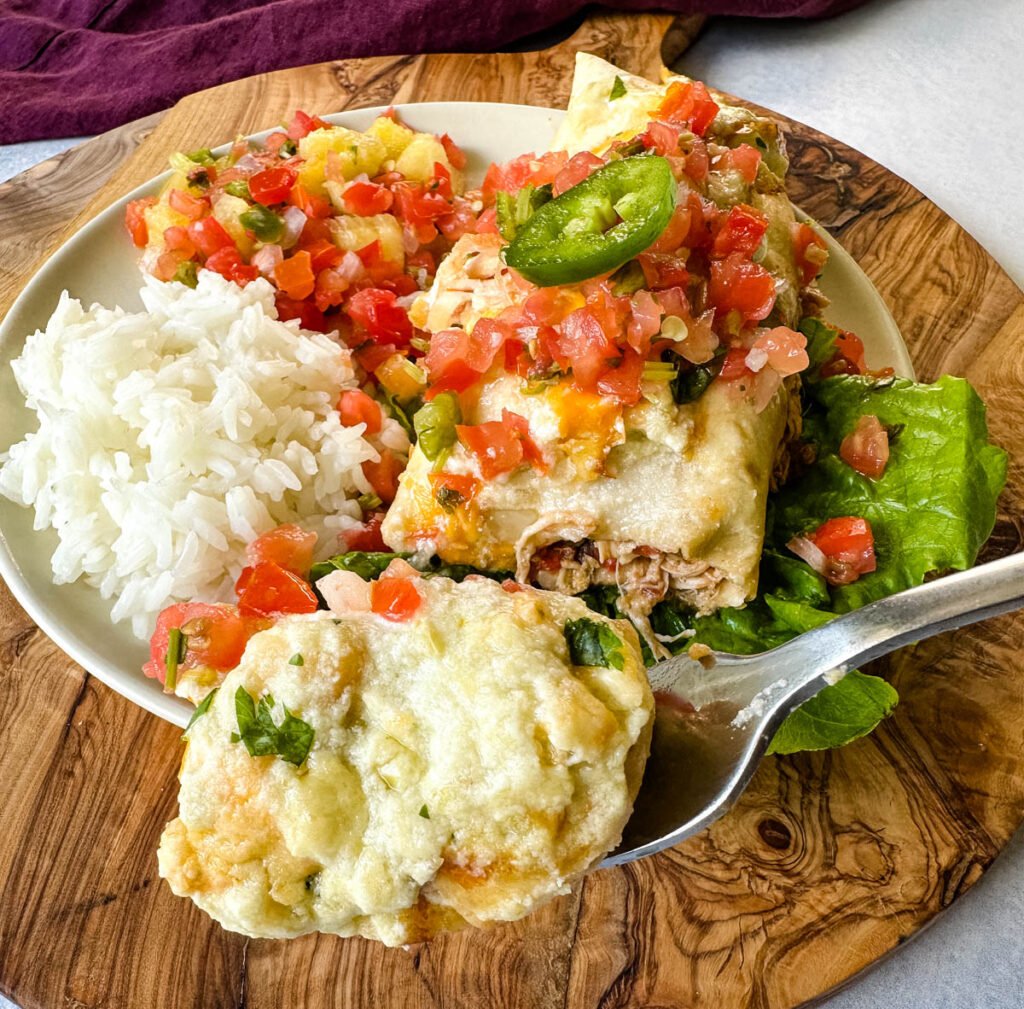 a spoonful of rotisserie chicken enchiladas on a plate with pico de gallo and jalapenos
