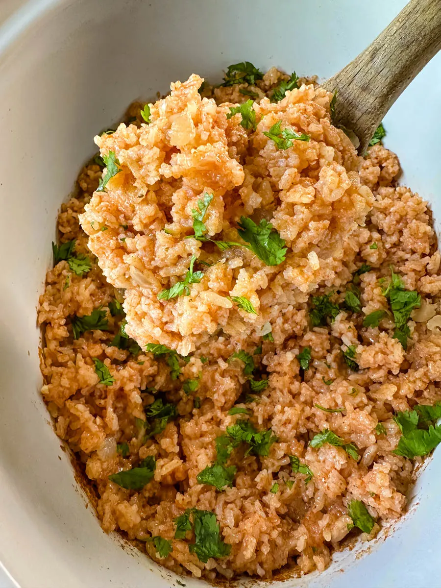 cooked Spanish Mexican rice in a white slow cooker Crockpot with a wooden spoon