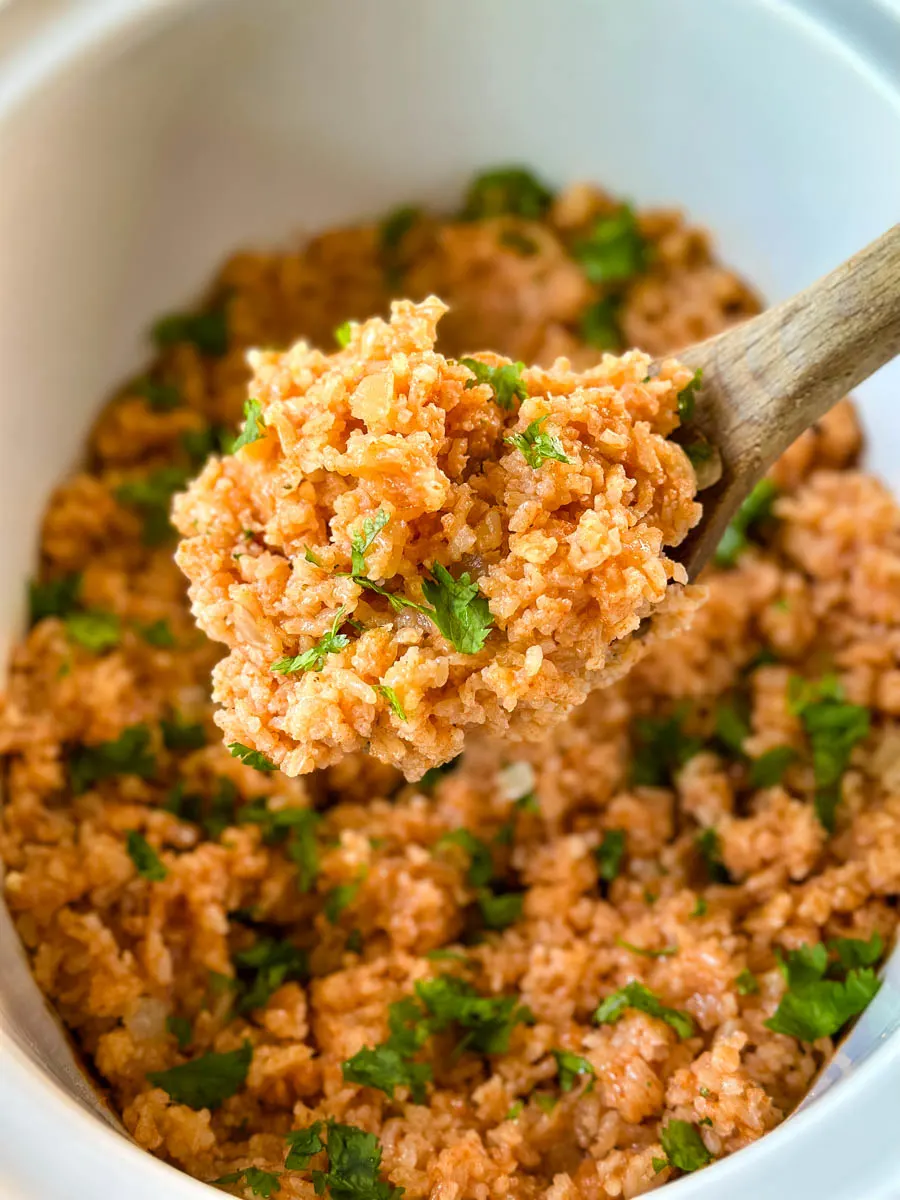 cooked Spanish Mexican rice in a white slow cooker Crockpot with a wooden spoon