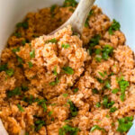 cooked Spanish Mexican rice in a white slow cooker Crockpot with a wooden spoon