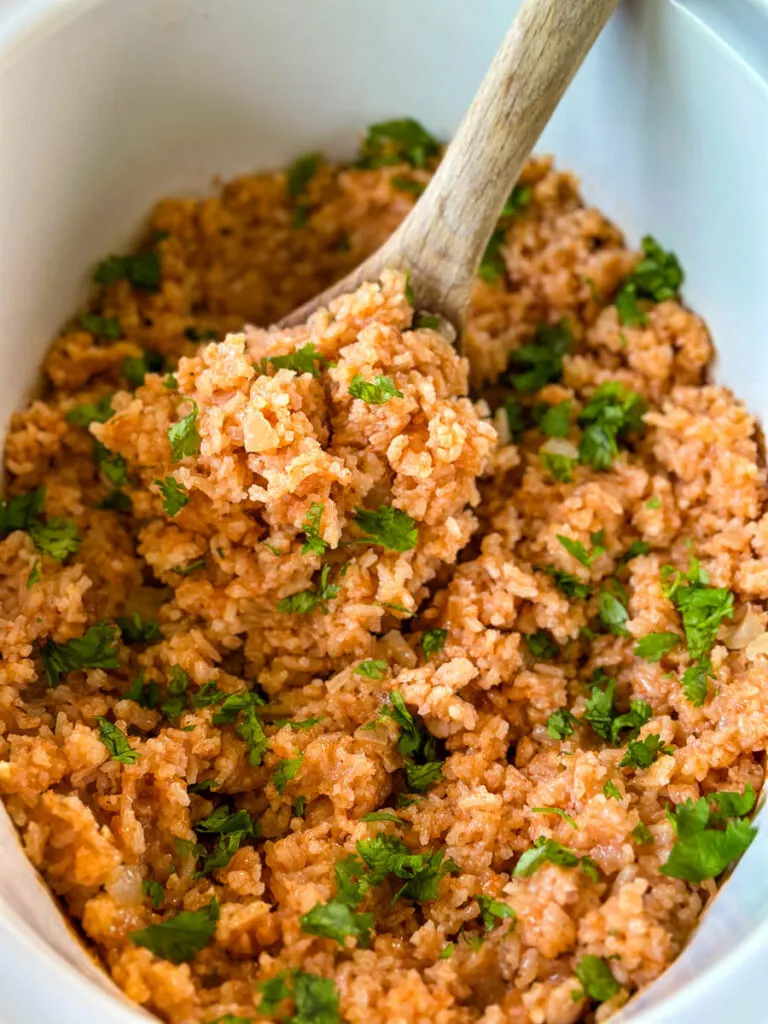 cooked Spanish Mexican rice in a white slow cooker Crockpot with a wooden spoon