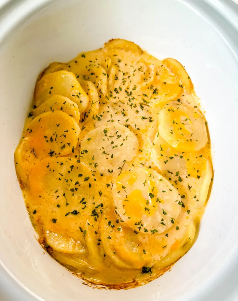 slow cooker cheesy potatoes in a white Crockpot with chives