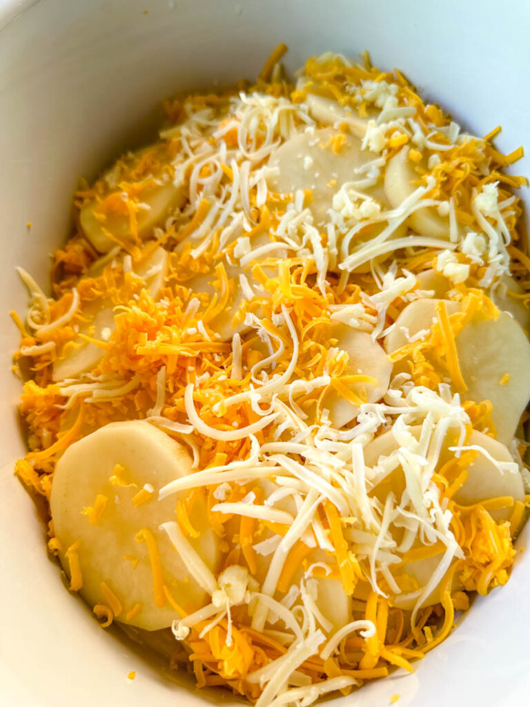 uncooked slow cooker cheesy potatoes in a white Crockpot