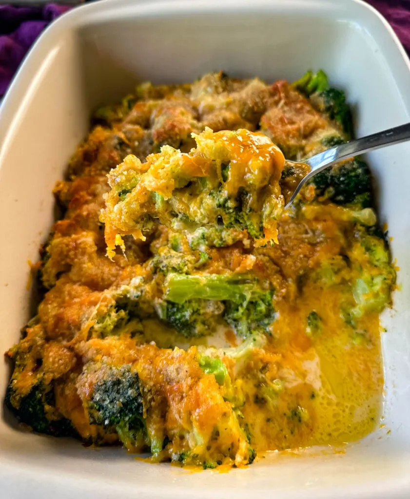 a fork full of broccoli au gratin with cheese and breadcrumbs in a baking dish