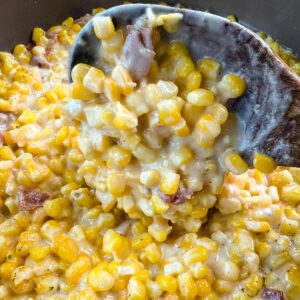 Southern creamed corn in a pot with a wooden spoon.