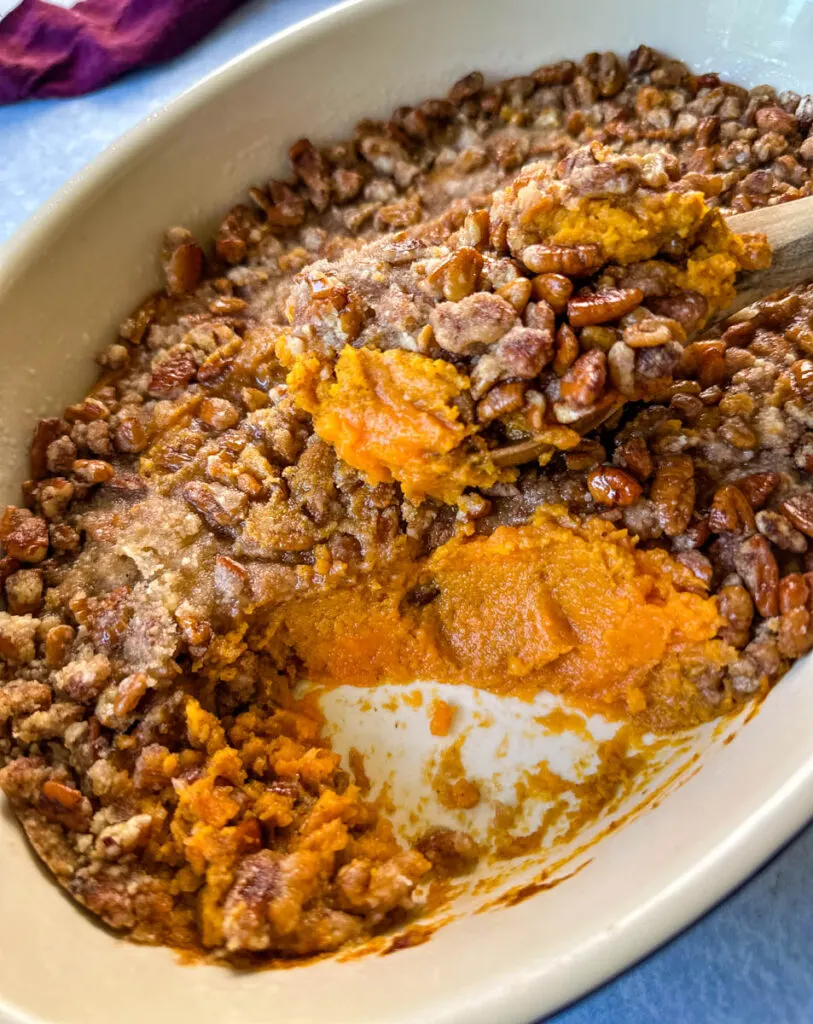 sweet potato casserole with pecans in a baking dish with a wooden spoon