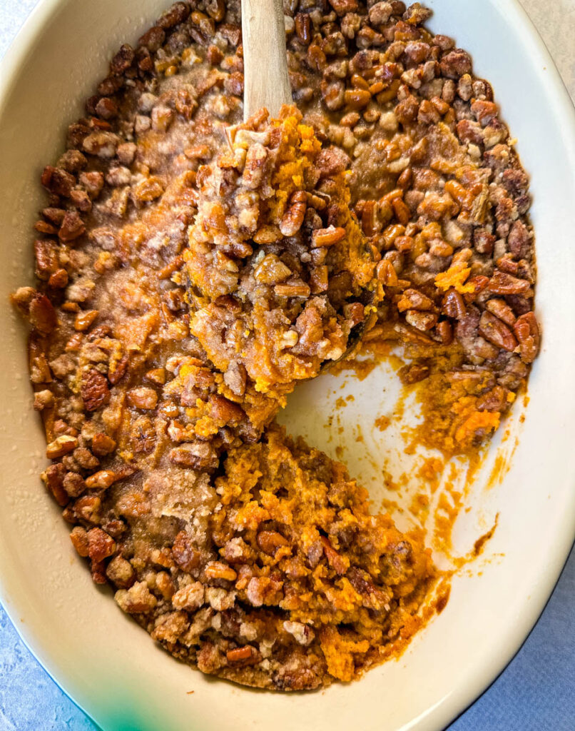 sweet potato casserole with pecans in a baking dish with a wooden spoon