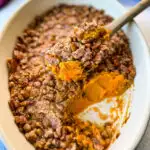 sweet potato casserole with pecans in a baking dish with a wooden spoon