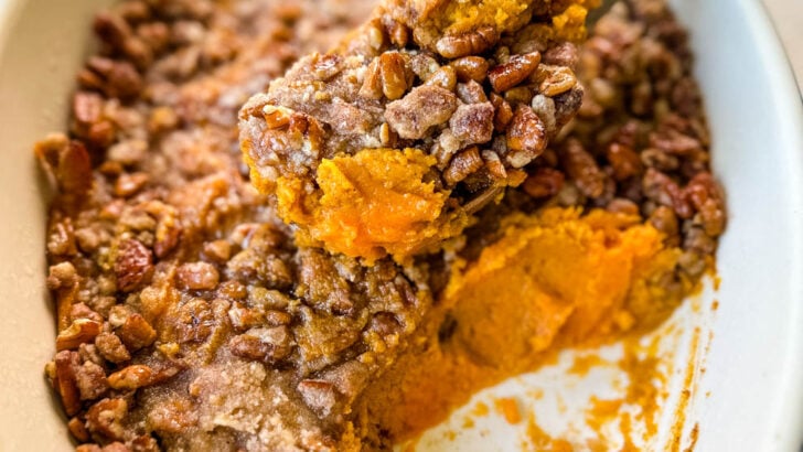 sweet potato casserole with pecans in a baking dish with a wooden spoon