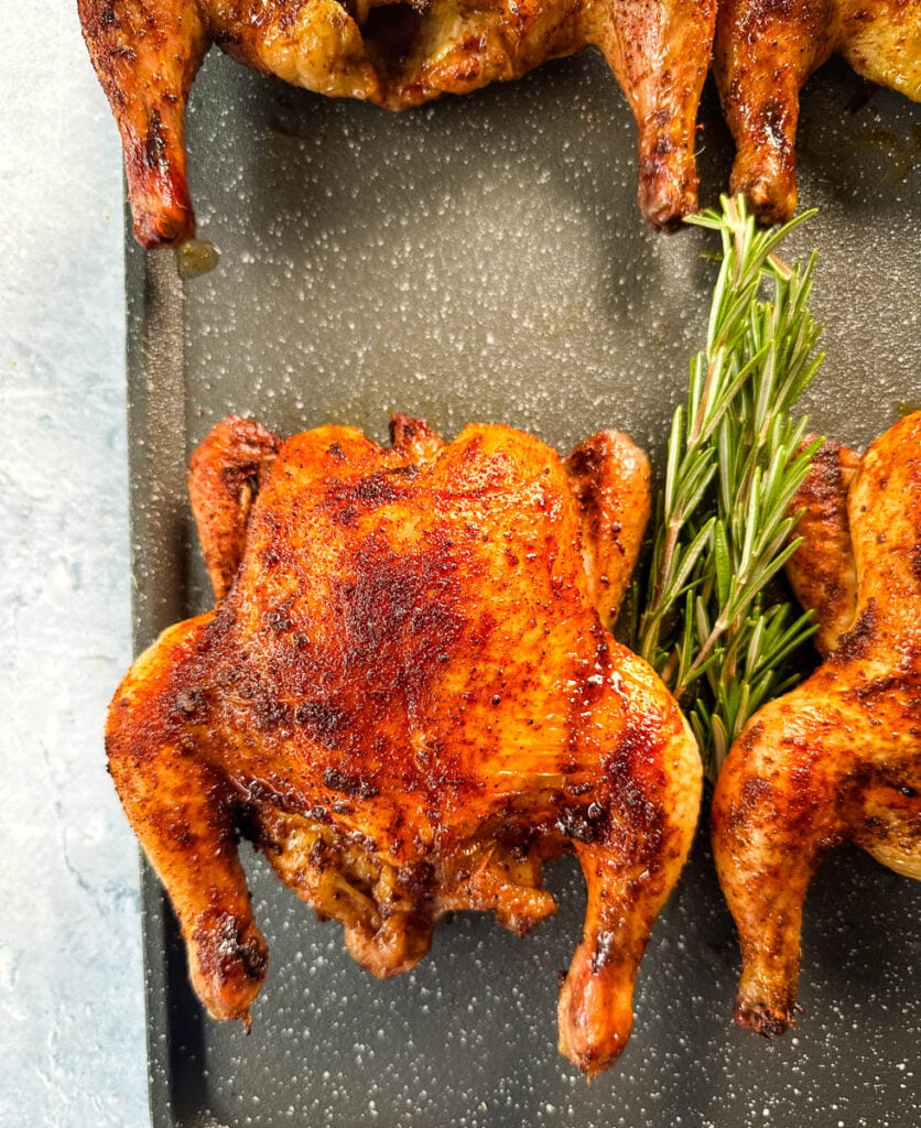 smoked Cornish hens on a sheet pan with fresh herbs