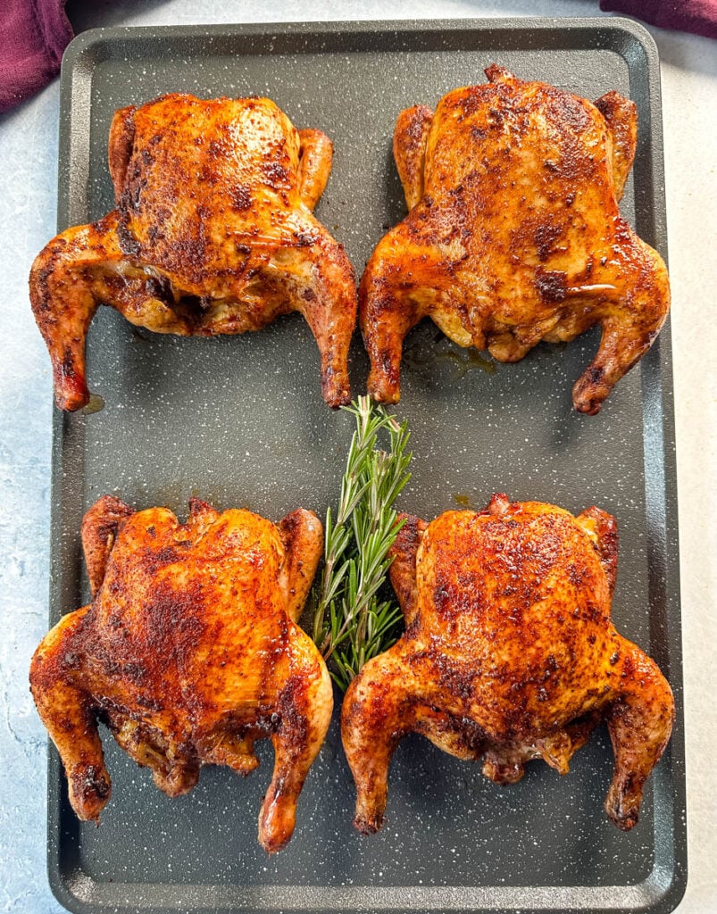 smoked Cornish hens on a sheet pan with fresh herbs