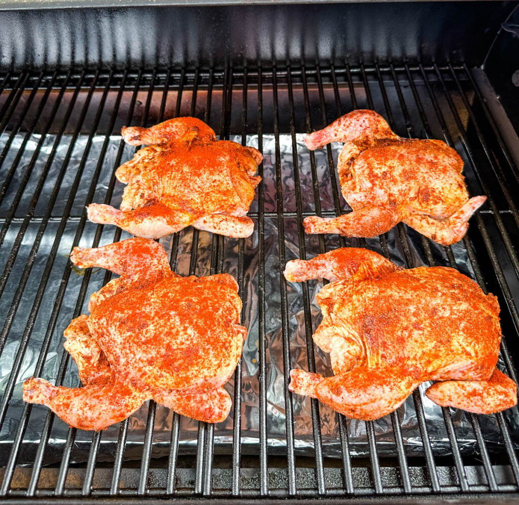 raw Cornish hens on a sheet pan with fresh herbs