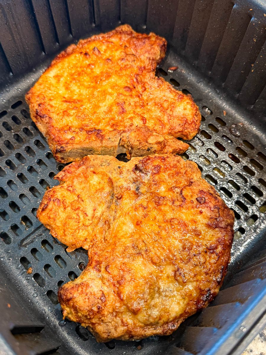 Two raw, breaded pork chops placed in the air fryer basket before cooking.