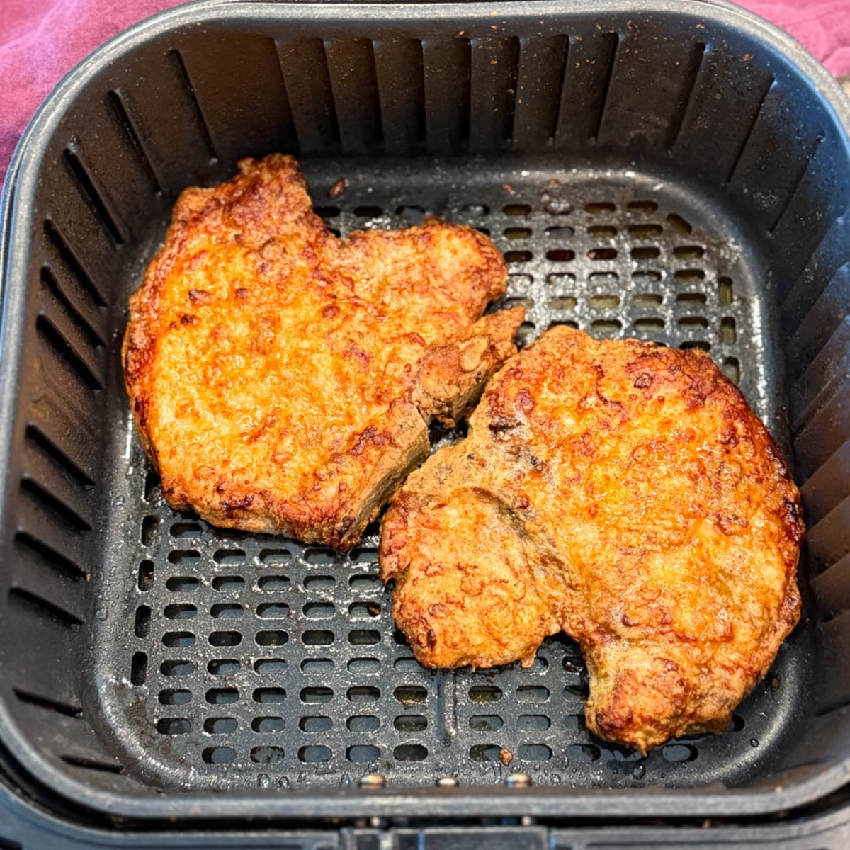 Two golden, crispy breaded pork chops sitting in an air fryer basket after cooking.