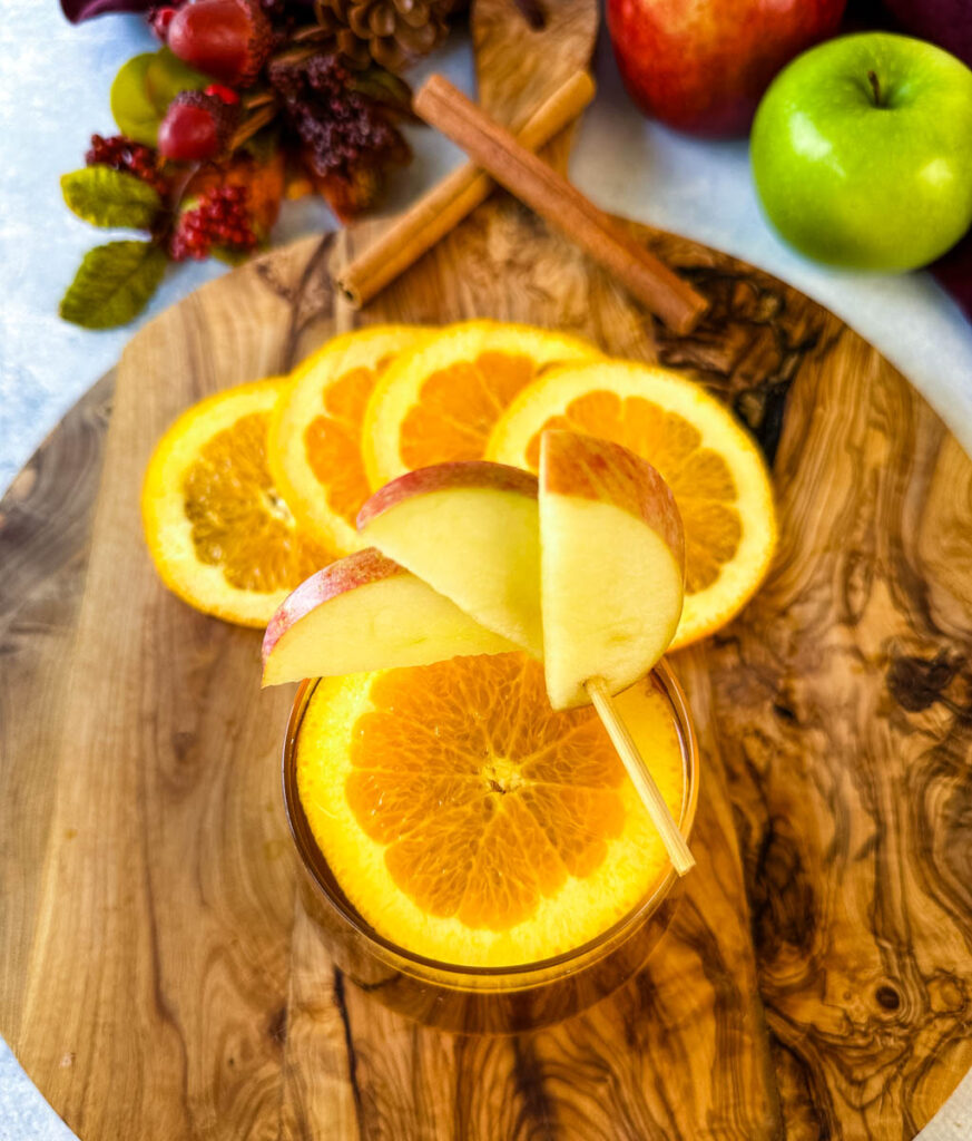 apple cider bourbon cocktail with orange and apple slices in a cup