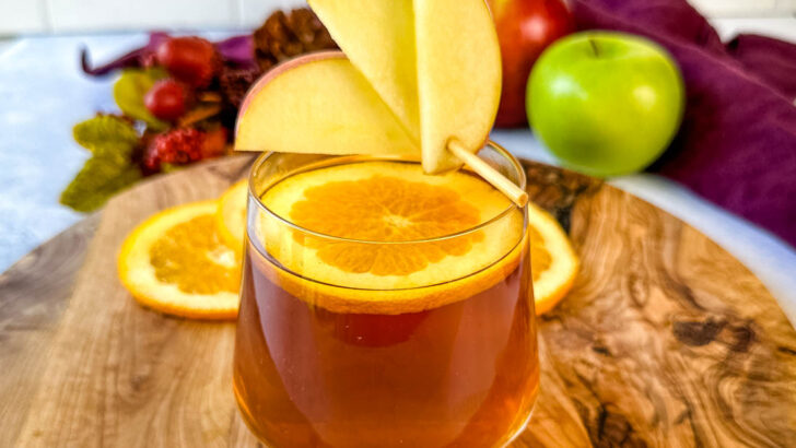 apple cider bourbon cocktail with orange and apple slices in a cup