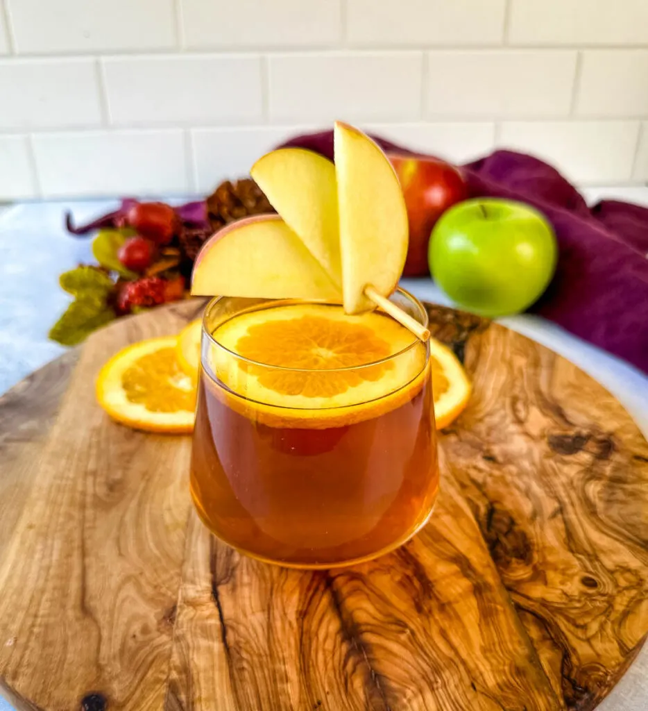 apple cider bourbon cocktail with orange and apple slices in a cup