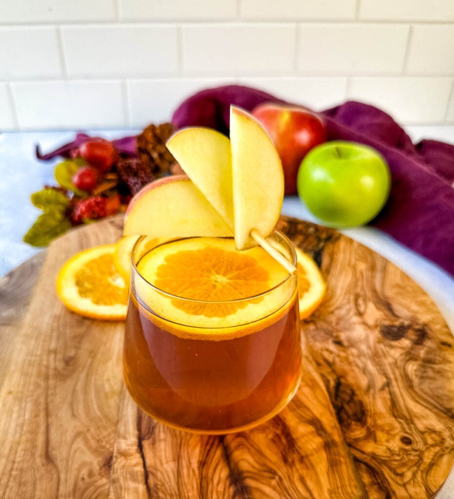 apple cider bourbon cocktail with orange and apple slices in a cup