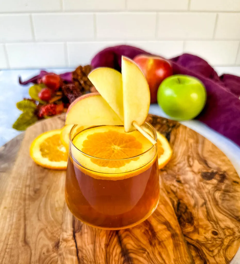 apple cider bourbon cocktail with orange and apple slices in a cup