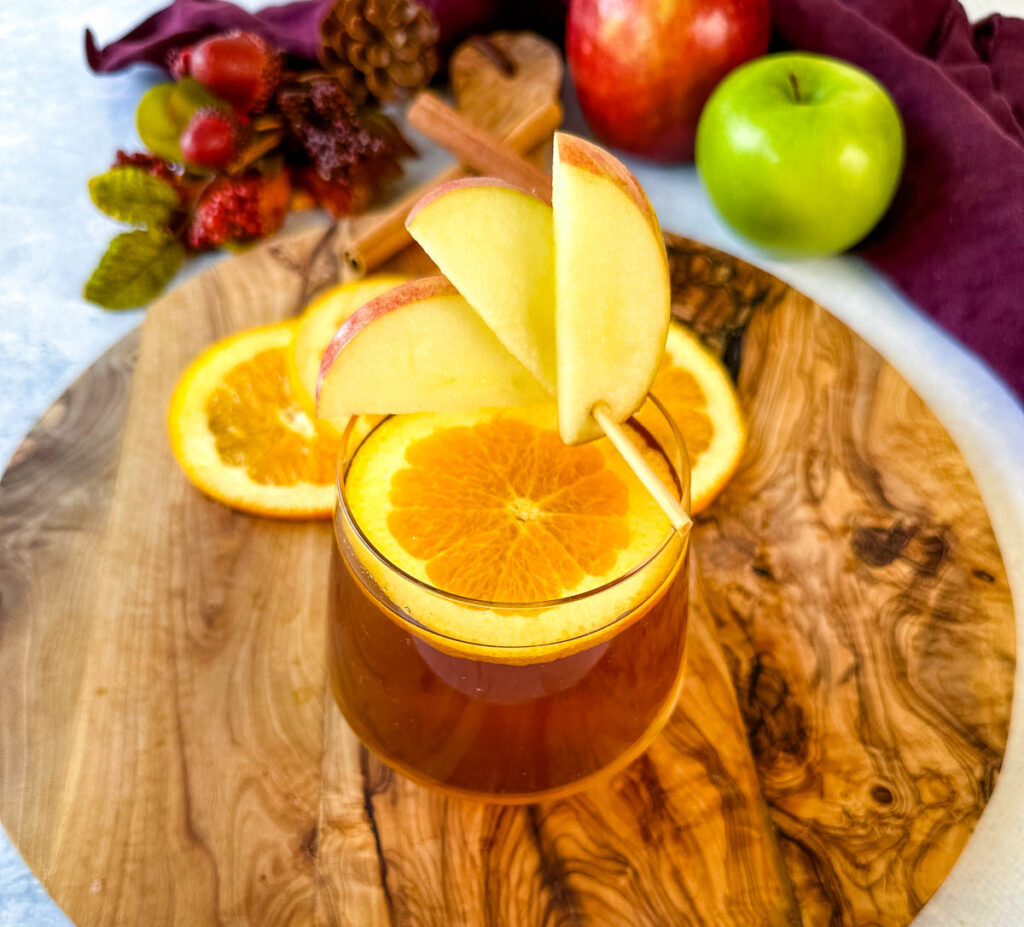apple cider bourbon cocktail with orange and apple slices in a cup